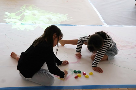 床一面に広がる紙には、プロジェクターで炎や植物が映し出され、児童は思い思いに絵を描きました