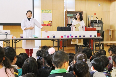 紫がいろいろな色に変化することを説明する白衣姿の小谷野先生